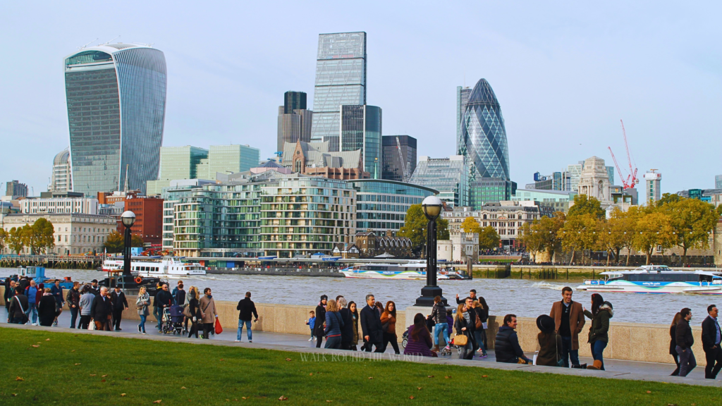 People walking along South Bank London with Thames river and city skyline in the background