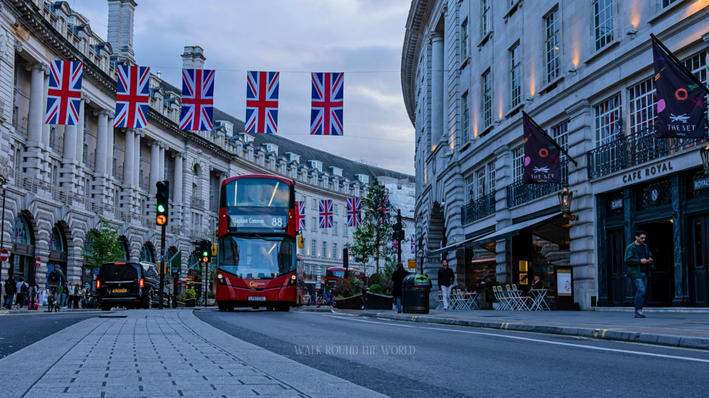 Iconic red double-decker bus driving through Central London street with historic buildings and city traffic