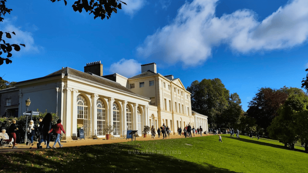 Kenwood House, a white neoclassical stately home on a grassy hill at Hampstead Heath, London, with visitors walking on a sunny day.