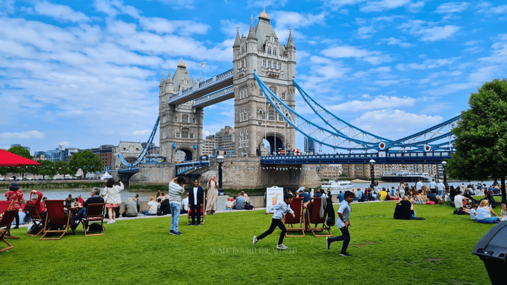Tower Bridge London in Summer with tourists relaxing beside the River Thames