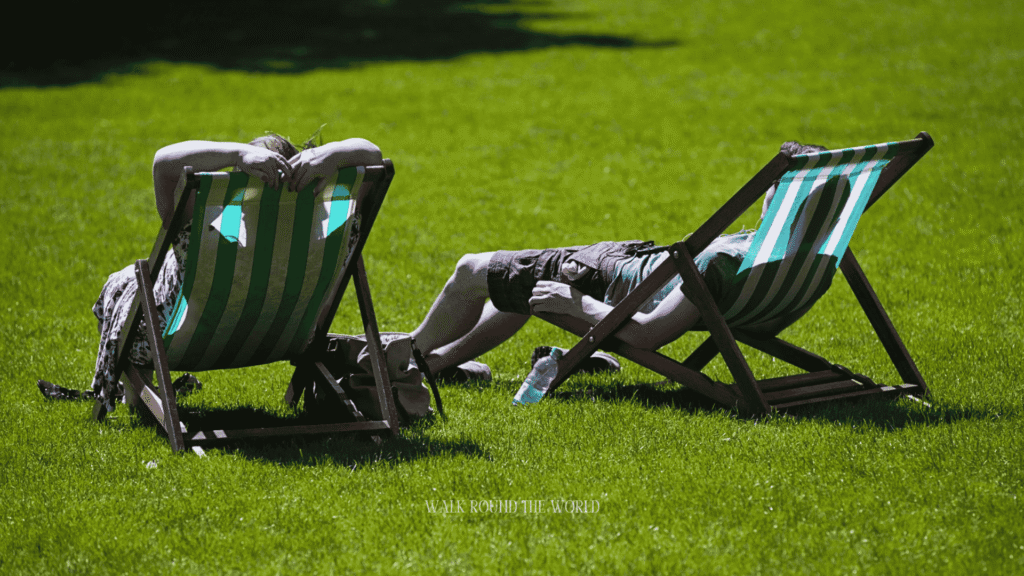 People relaxing on deck chairs in a London park during a warm summer afternoon