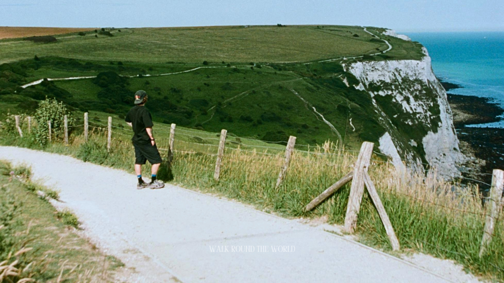 A visitor walking along the scenic White Cliffs of Dover coastal path overlooking the English Channel during a day trip from London.