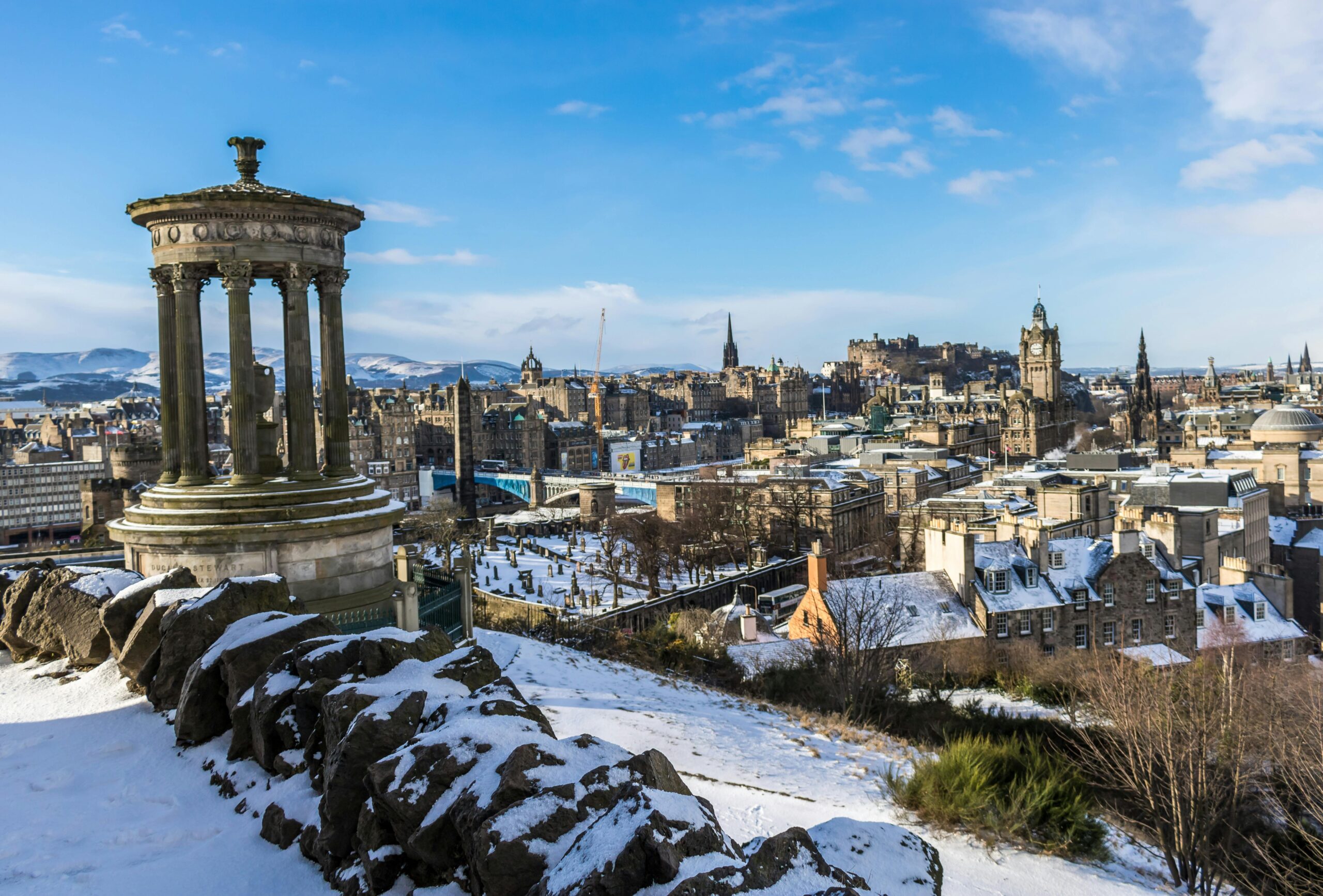 A winter view of Edinburgh from Calton Hill, featuring snow-covered cityscape and historical landmarks.
