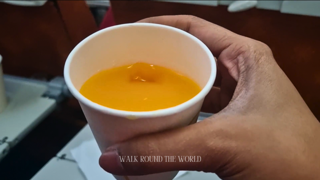 Passenger holding a glass of orange juice and roasted crunchy corn snack served on Air India economy class flight AI 133